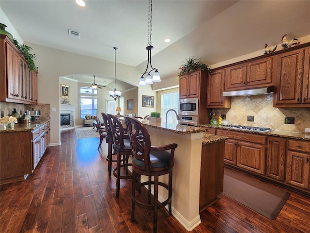 kitchen featuring a kitchen island with sink, a kitchen breakfast bar, stone counters, and appliances with stainless steel finishes