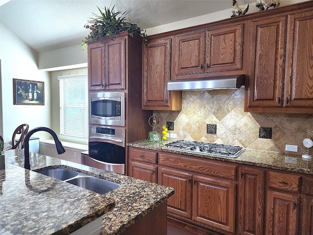 kitchen featuring wall chimney exhaust hood, sink, dark stone countertops, stainless steel appliances, and decorative backsplash