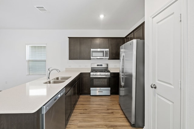 kitchen featuring appliances with stainless steel finishes, sink, dark brown cabinetry, kitchen peninsula, and light hardwood / wood-style flooring