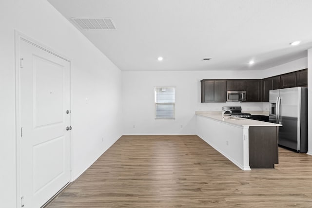 kitchen featuring appliances with stainless steel finishes, kitchen peninsula, dark brown cabinets, and light hardwood / wood-style flooring