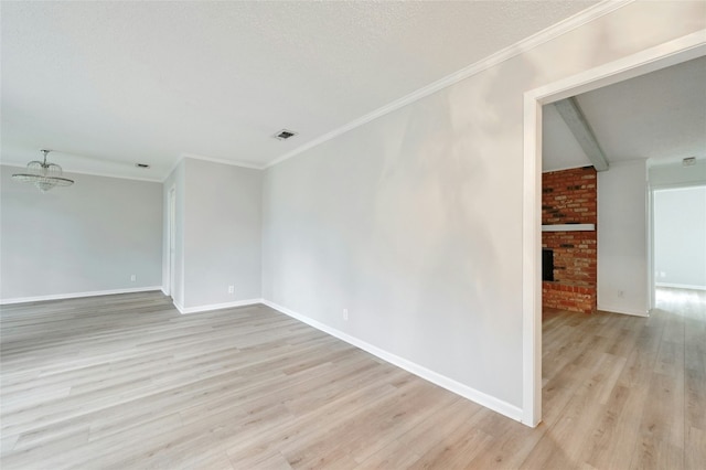 spare room featuring beam ceiling, a textured ceiling, a brick fireplace, and light hardwood / wood-style flooring