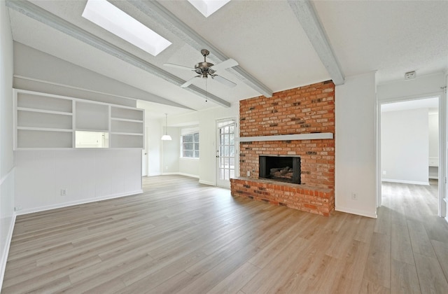 unfurnished living room with vaulted ceiling with skylight, a textured ceiling, light wood-type flooring, ceiling fan, and a fireplace