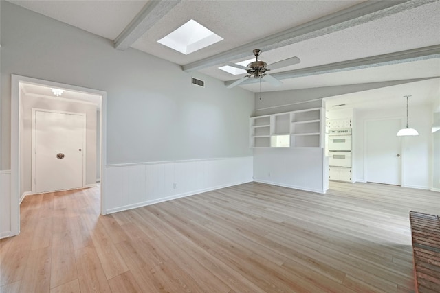 unfurnished living room with lofted ceiling with skylight, ceiling fan, a textured ceiling, and light hardwood / wood-style flooring