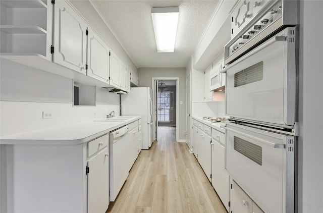 kitchen with sink, a textured ceiling, light wood-type flooring, white appliances, and white cabinets