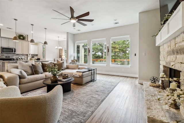 living room with sink, a fireplace, ceiling fan with notable chandelier, and light hardwood / wood-style flooring