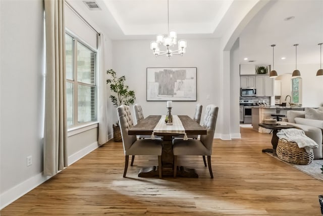 dining room with a notable chandelier, a tray ceiling, light hardwood / wood-style floors, and sink