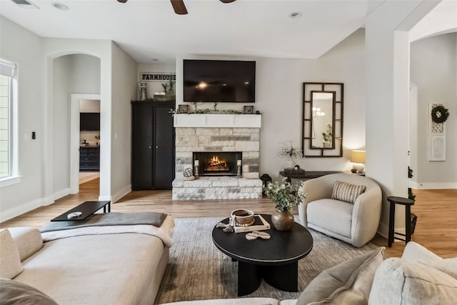 living room with ceiling fan, a stone fireplace, and light hardwood / wood-style floors