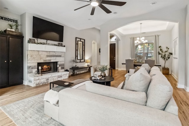 living room with a fireplace, a raised ceiling, ceiling fan with notable chandelier, and light hardwood / wood-style flooring