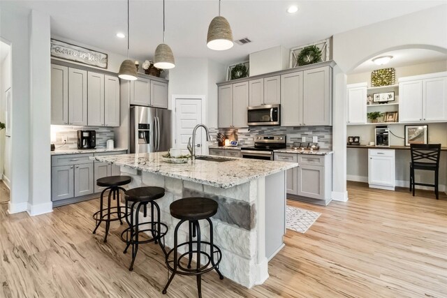 kitchen with appliances with stainless steel finishes, sink, gray cabinetry, and a kitchen island with sink