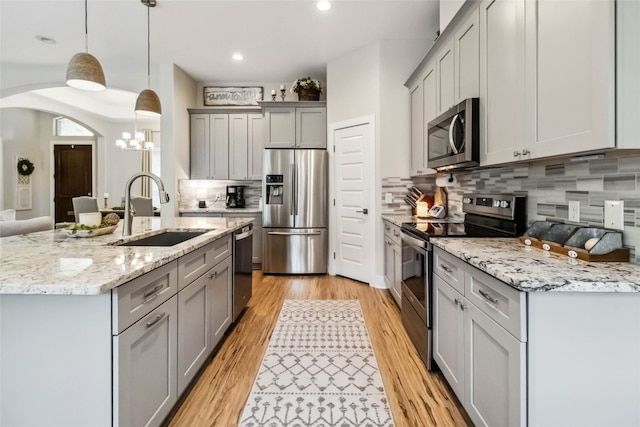 kitchen featuring sink, gray cabinetry, hanging light fixtures, stainless steel appliances, and light wood-type flooring