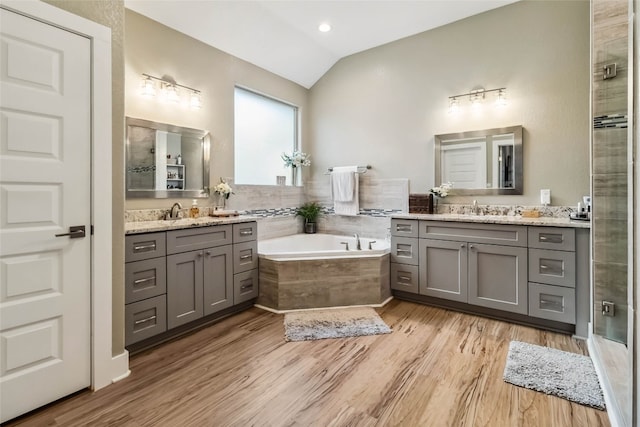 bathroom featuring vanity, separate shower and tub, vaulted ceiling, and wood-type flooring