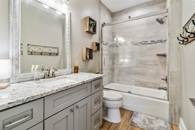 full bathroom featuring wood-type flooring, combined bath / shower with glass door, vanity, and toilet