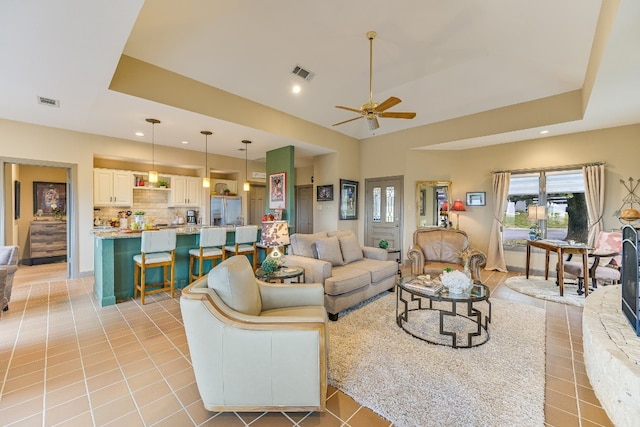 tiled living room with ceiling fan and a tray ceiling