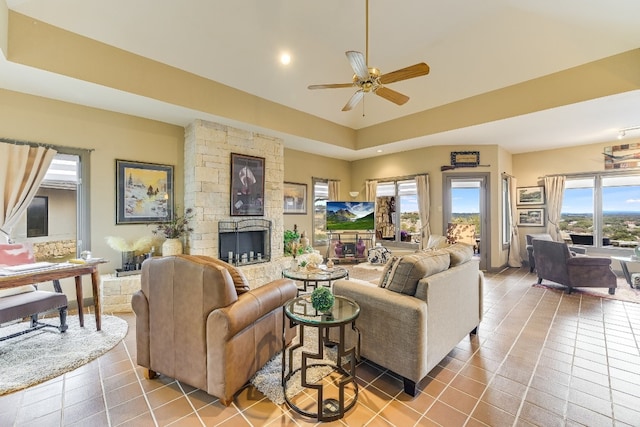 tiled living room featuring a tray ceiling, a fireplace, and ceiling fan