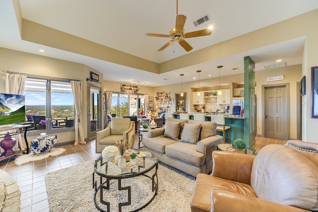 living room with a raised ceiling, light tile patterned floors, and ceiling fan