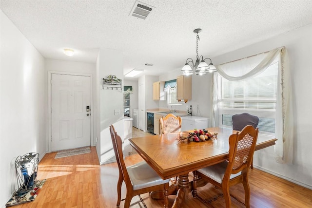 dining space featuring sink, light hardwood / wood-style floors, a textured ceiling, and a notable chandelier