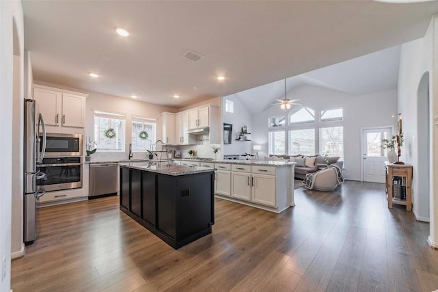 kitchen featuring dark wood-type flooring, white cabinetry, stainless steel appliances, light stone countertops, and a kitchen island