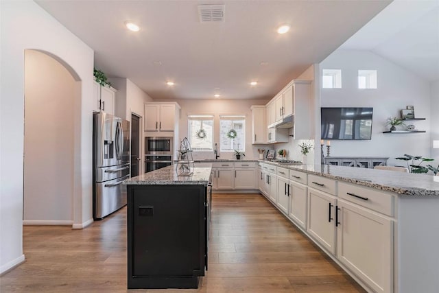 kitchen with white cabinetry, a center island with sink, appliances with stainless steel finishes, light stone countertops, and light hardwood / wood-style floors