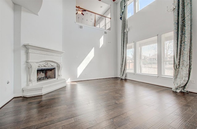 unfurnished living room with dark hardwood / wood-style floors, a high end fireplace, and a towering ceiling