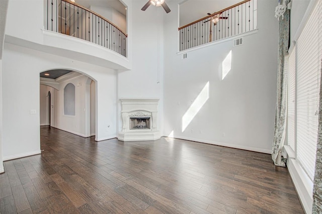 unfurnished living room with dark wood-type flooring, ceiling fan, a fireplace, and a towering ceiling