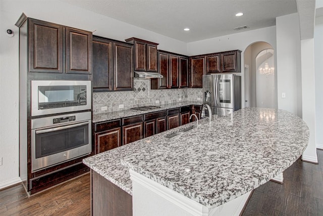 kitchen with an island with sink, appliances with stainless steel finishes, light stone counters, and dark brown cabinetry