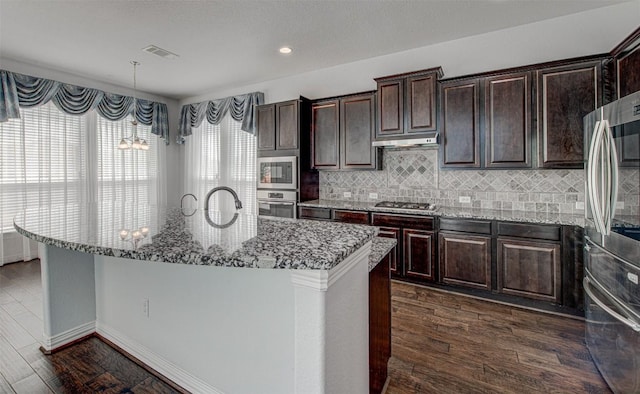 kitchen featuring dark brown cabinetry, decorative light fixtures, an island with sink, and appliances with stainless steel finishes