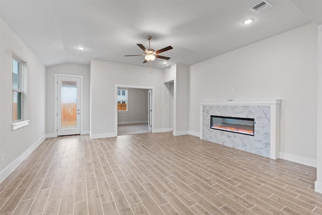 unfurnished living room with ceiling fan, vaulted ceiling, a high end fireplace, and light hardwood / wood-style floors