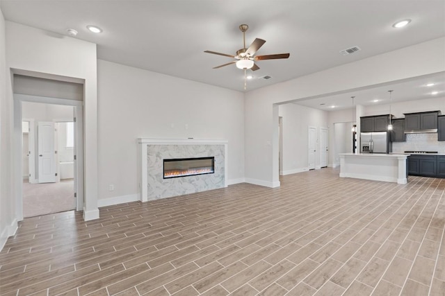 unfurnished living room with a premium fireplace, ceiling fan, and light wood-type flooring