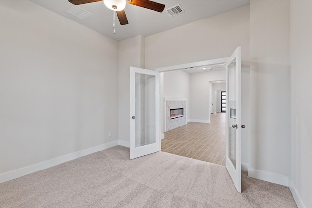 spare room featuring french doors, light colored carpet, a fireplace, and ceiling fan