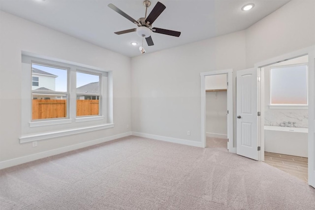 unfurnished bedroom with ensuite bathroom, a walk in closet, ceiling fan, light carpet, and a closet