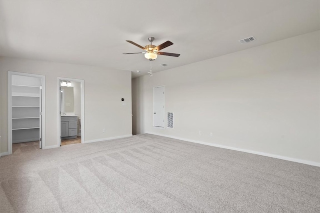 unfurnished bedroom featuring light colored carpet, baseboards, a walk in closet, and visible vents