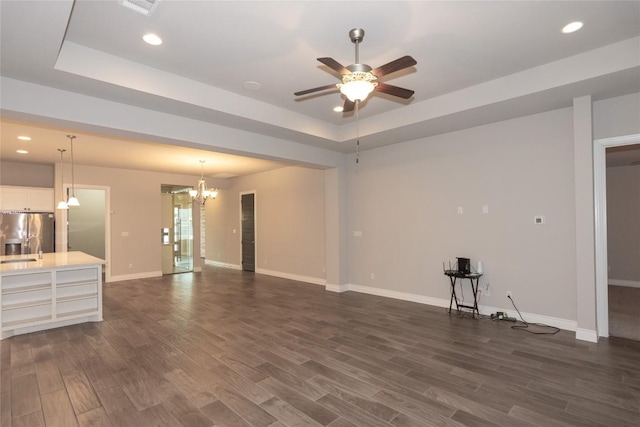 unfurnished living room featuring a tray ceiling, dark hardwood / wood-style flooring, and ceiling fan with notable chandelier