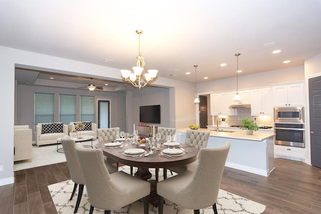 dining room featuring ceiling fan with notable chandelier, sink, and dark wood-type flooring