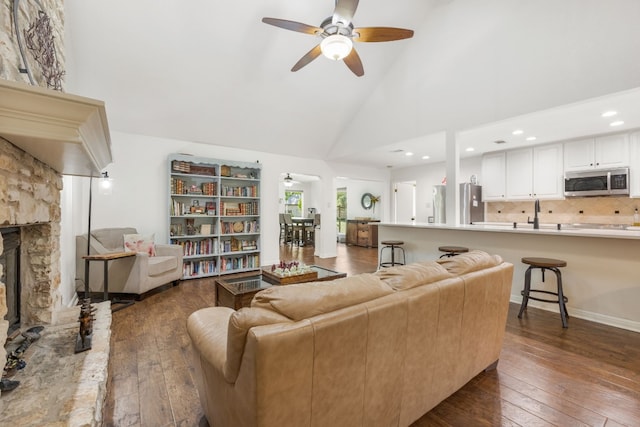 living room featuring wood-type flooring, ceiling fan, a fireplace, and high vaulted ceiling