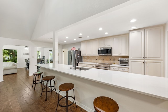 kitchen with sink, stainless steel appliances, a kitchen breakfast bar, tasteful backsplash, and dark hardwood / wood-style flooring