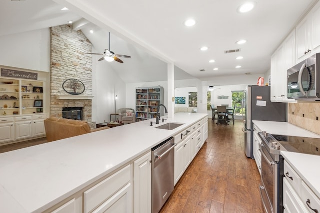 kitchen featuring sink, white cabinetry, stainless steel appliances, dark hardwood / wood-style floors, and a stone fireplace