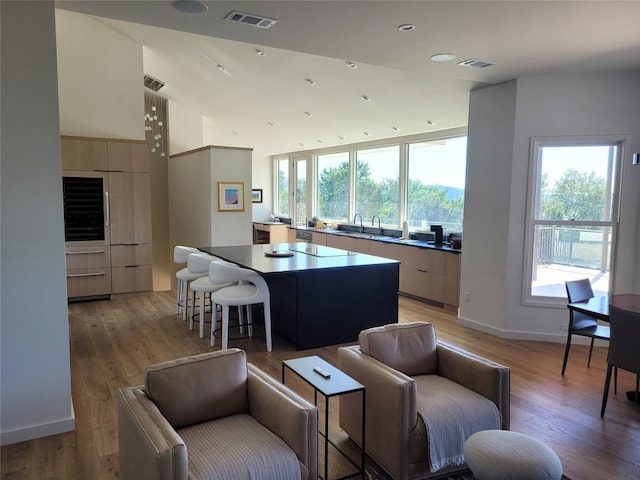 kitchen featuring cooktop, sink, light brown cabinets, a kitchen island, and light hardwood / wood-style floors