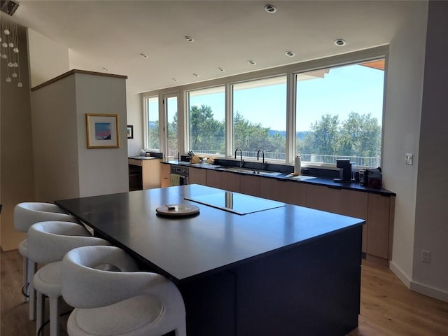 kitchen with black electric stovetop, sink, a kitchen island, and light hardwood / wood-style flooring