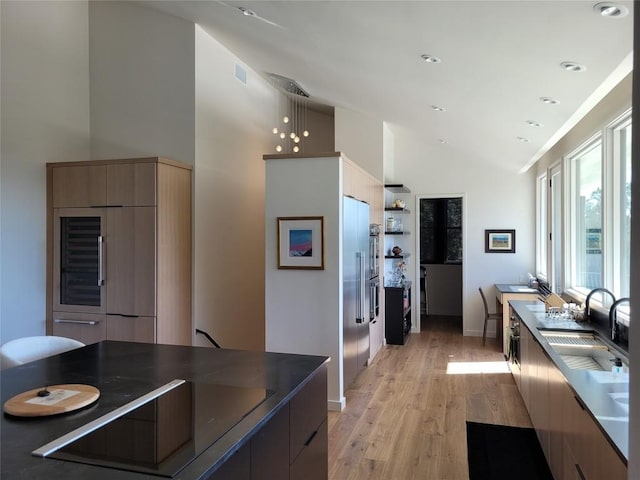 kitchen with sink, high vaulted ceiling, hanging light fixtures, light wood-type flooring, and black stovetop