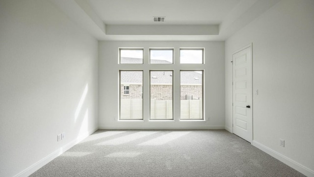 unfurnished room featuring a tray ceiling, carpet, visible vents, and baseboards