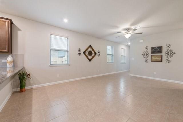 spare room featuring ceiling fan, plenty of natural light, light tile patterned flooring, and baseboards