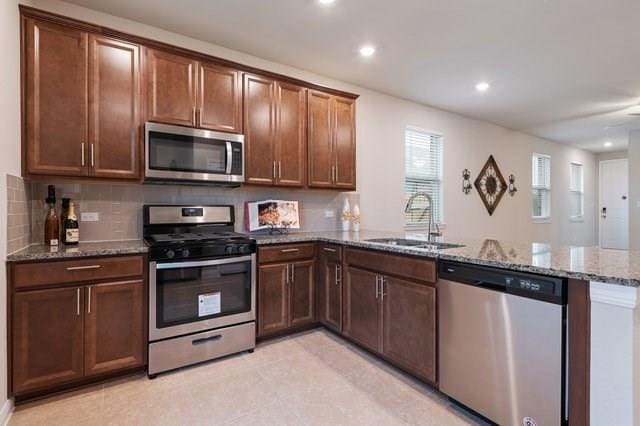 kitchen with stone countertops, stainless steel appliances, a peninsula, a sink, and tasteful backsplash