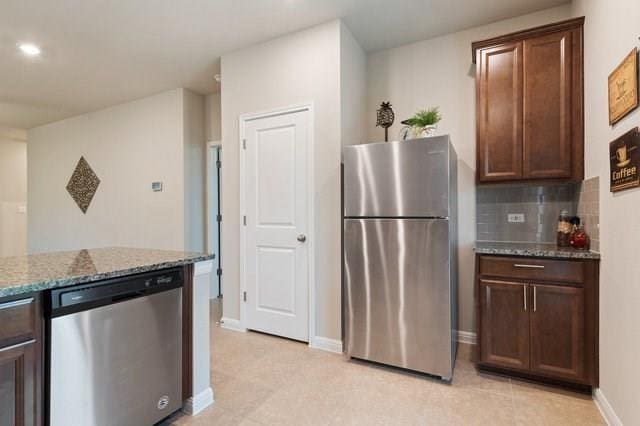 kitchen featuring dark brown cabinetry, baseboards, appliances with stainless steel finishes, dark stone counters, and tasteful backsplash