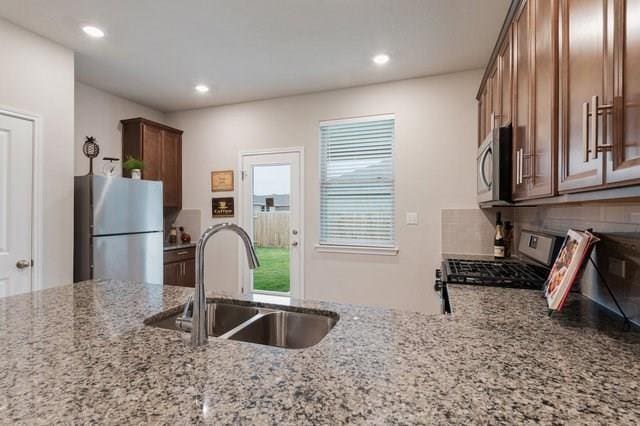 kitchen featuring a sink, light stone countertops, stainless steel appliances, backsplash, and recessed lighting