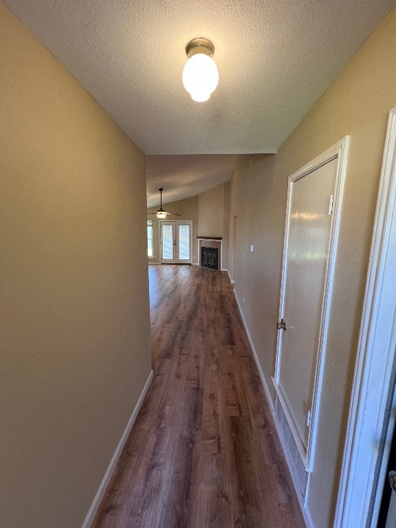 hallway with lofted ceiling, dark wood-type flooring, and a textured ceiling