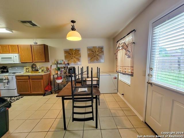 kitchen featuring light tile patterned floors, white appliances, decorative light fixtures, and a kitchen breakfast bar