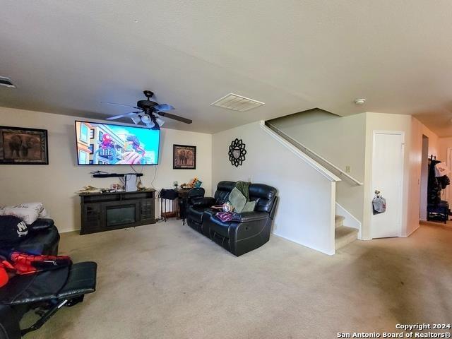 carpeted living room with ceiling fan and a fireplace