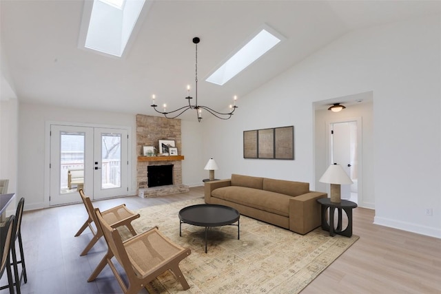 living room with a stone fireplace, a chandelier, a skylight, high vaulted ceiling, and light wood-type flooring