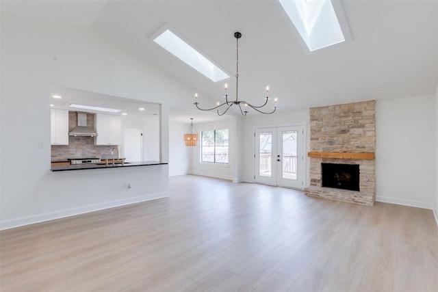 unfurnished living room with a stone fireplace, high vaulted ceiling, a skylight, a chandelier, and light wood-type flooring