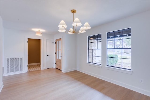 empty room featuring a chandelier and light hardwood / wood-style floors